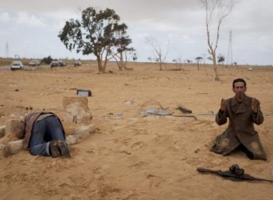 A Libyan rebel prays next to his gun while another kneels over the grave of his brother who was killed in fighting on the outskirts of Adjabiya, south of Benghazi.