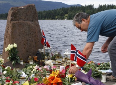 A man places a Norwegian flag between flowers in Utvika in front of Utoya island