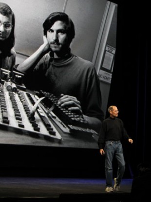 Steve Jobs makes a presentation last year in front of a photograph of himself as a younger man, at the startup of Apple.