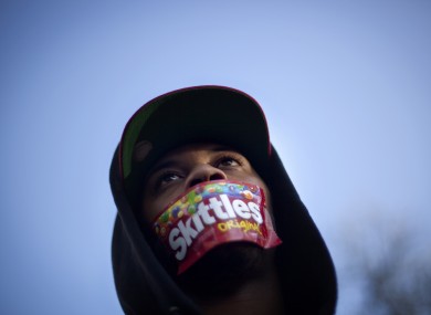 A man attending a rally wears a Skittles wrapper over his mouth. Trayvon Martin was said to be carrying Skittles and ice tea as well as wearing a hoodie when he died.