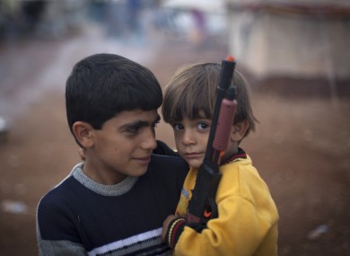 Two Syrian boys who fled with their families from the violence in their village, look on as one holds a gun toy at a displaced camp, in the Syrian village of Atmeh, near the Turkish border with Syria.