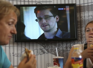 Wednesday, June 26, 2013 file photo transit passengers eat at a cafe with a TV screen with a news program showing a report on Edward Snowden