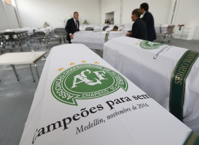 Funeral employees arrange caskets covered in white sheets with a Chapecoense soccer team logo.