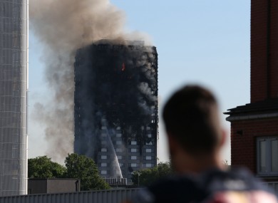 A man watches smoke pouring from a fire that has engulfed the 27-storey Grenfell Tower in west London.