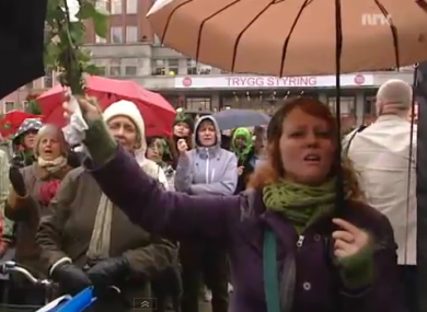 A woman holds a rose as she sings along to 'Barn av regnbuen' at Youngstorget in Oslo.
