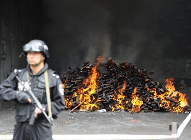 An officer guards a burning pile of guns in Yuxi, Tunnan Province.