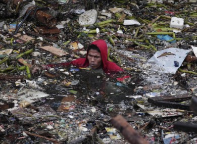 A Manila resident swims in polluted water as he attempts to salvage items from his destroyed home.