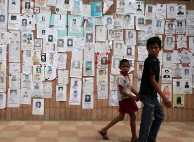 Two boys walk past a wall showing flyers of missing people near the collapsed factory in Bangladesh