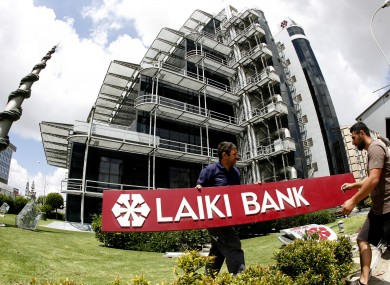 Workers take down the signs at the headquarters of Cyprus' now defunct bank Laiki in Nicosia today.