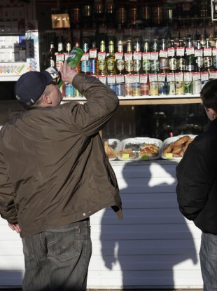 File: A Russian man drinks from a bottle standing in front of a liquor booth in a street in Moscow