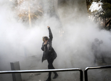 A university student attends a protest inside Tehran University earlier this week while a smoke grenade is thrown by anti-riot police.