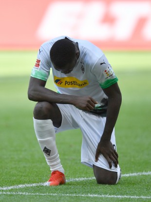 Mönchengladbach's Marcus Thuram kneels on the grass after his opening goal.