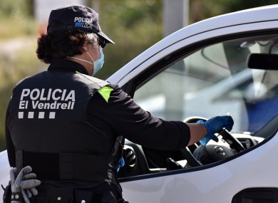 A police officer wearing a surgical mask verifies the identification of a driver at a mobility checkpoint to ensure compliance with the rules of confinement.