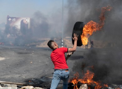 A Palestinian protester rolls a burning tyre towards Israeli army soldiers during clashes at the northern entrance of the West Bank city of Ramallah