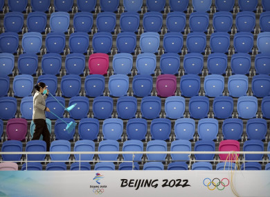 A maintenance worker walks through an empty section of spectator stands near a logo for the Beijing 2022 Winter Olympics.