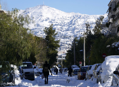 People walk on a frozen road after a snowstorm as Penteli mountain is seen in the background, in northern Athens, Greece,